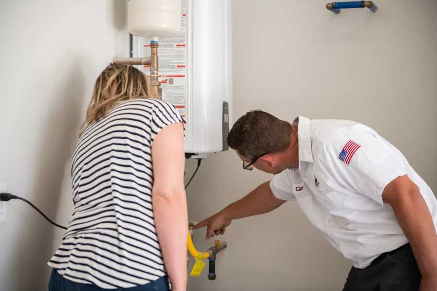 Thompson Plumbing technician Carlin inspecting tankless water heater connections and valves with a St. George Utah homeowner on-site