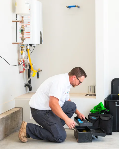 Thompson Plumbing technician kneeling next to a tankless water heater installation inside a St. George Utah home