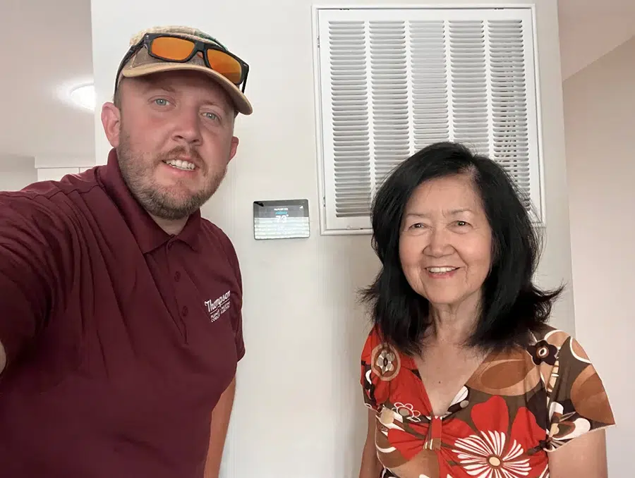 Thompson technician and happy customer posing by a newly installed smart thermostat in St. George, Utah.