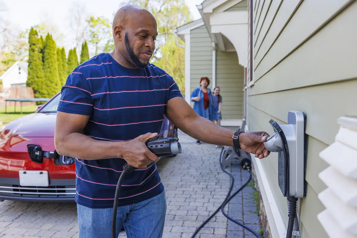 A man connects an electric vehicle charging cable to a wall-mounted home EV charger on the side of a St George Utah area house